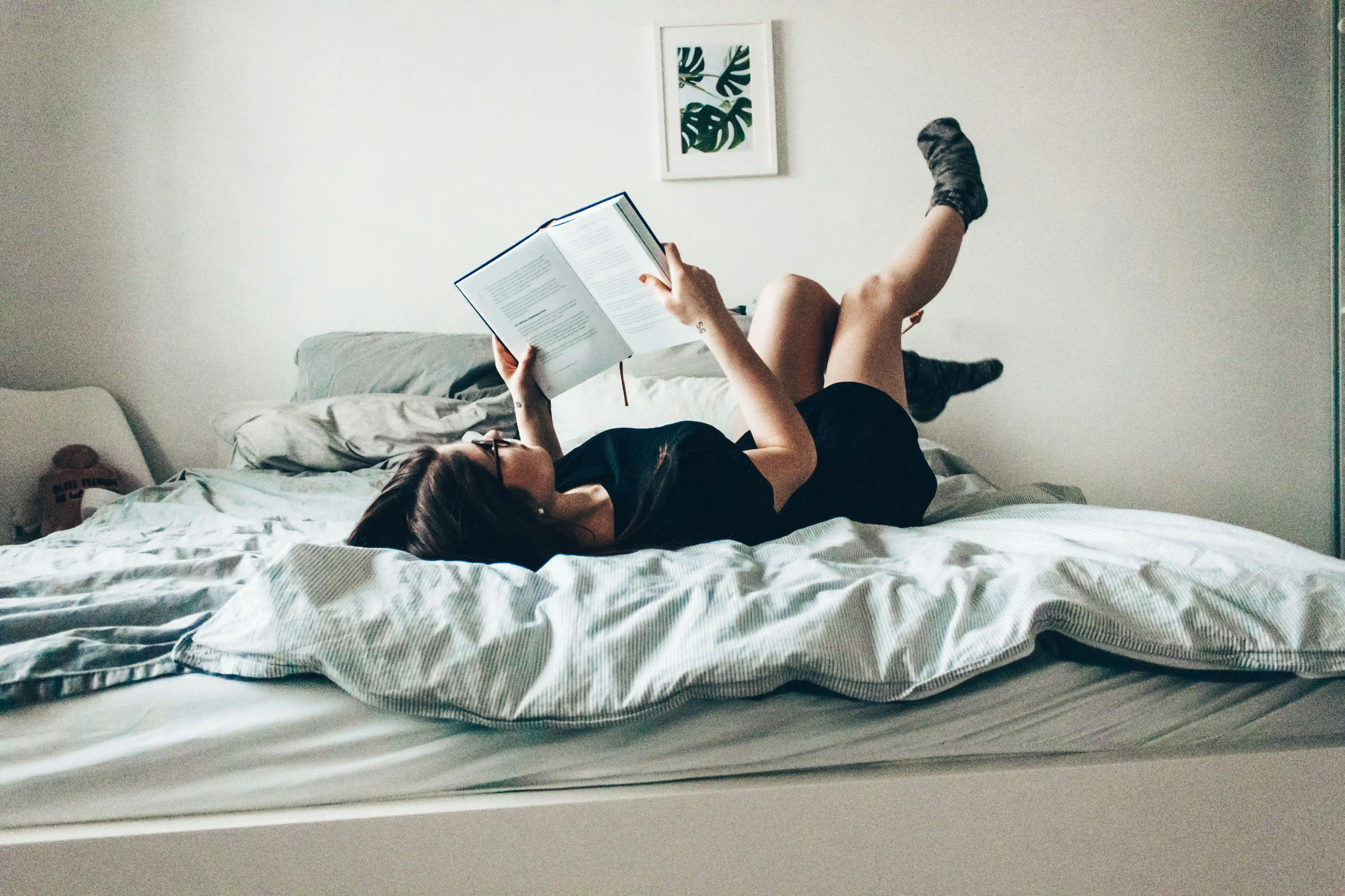 a women laying on her bed, reading a book